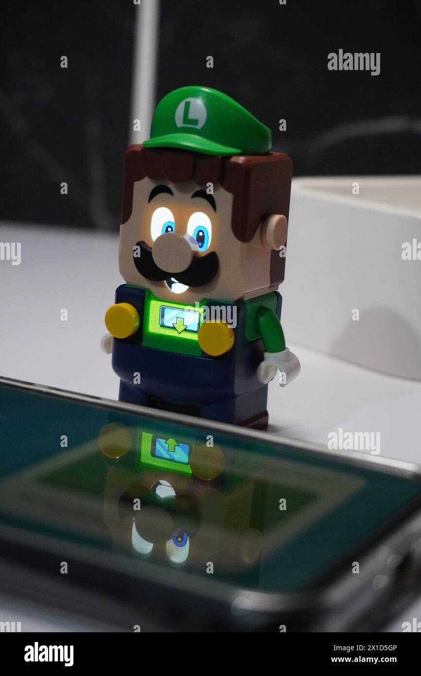 Una figura di Luigi del cartone animato di Super Mario Bros che si illumina e si trova vicino ad un cellulare illuminato Foto Stock