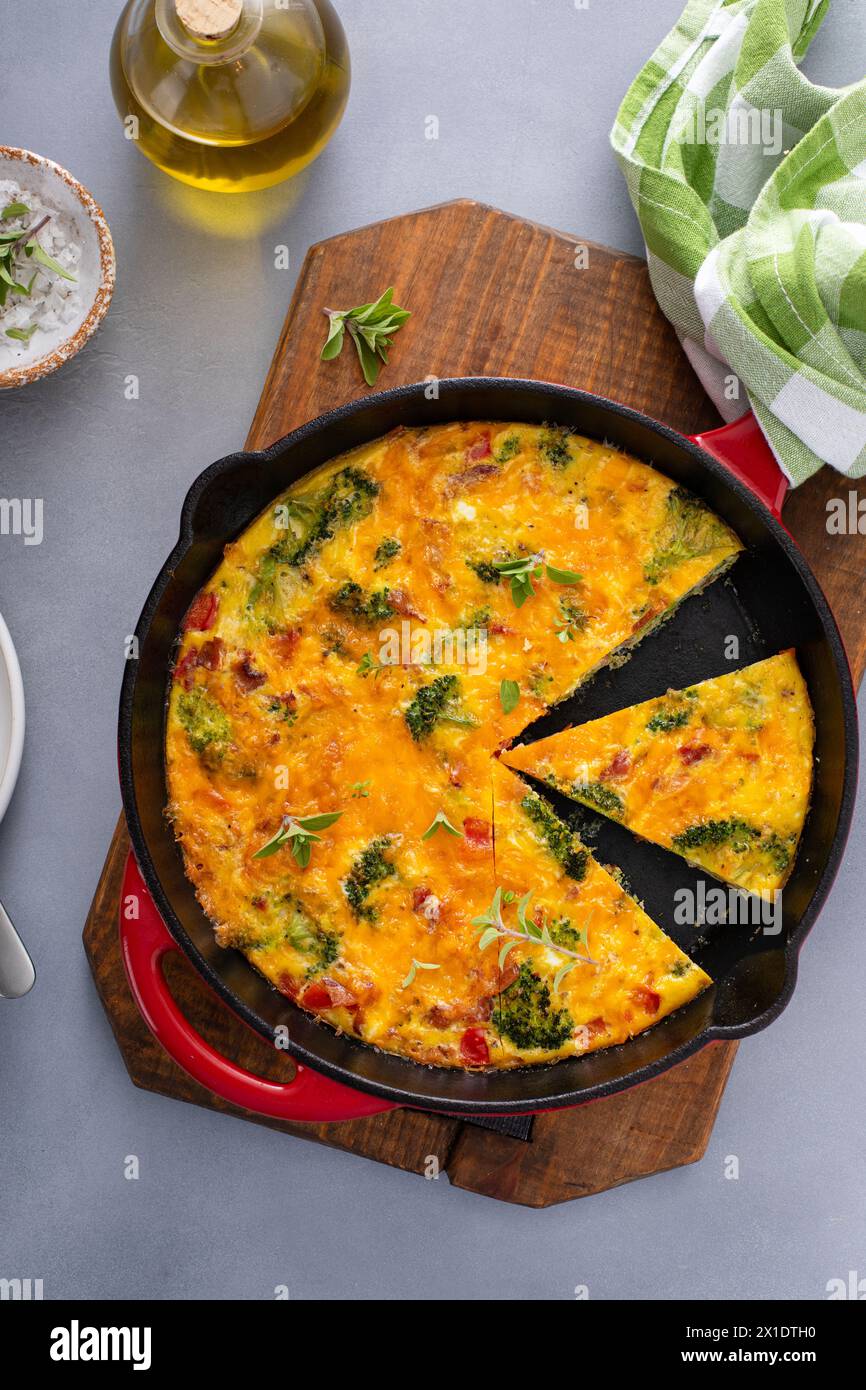 Frittata sana o quiche con broccoli e pepe rosso, condita con formaggio cheddar e pancetta tagliata in una padella di ghisa Foto Stock