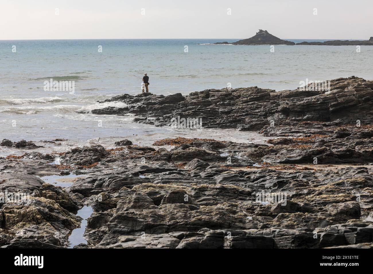 Pescatore solitario che pesca sulle rocce a Kenneggy Sand o Kenneggy Sands, una spiaggia remota nel sud-ovest della Cornovaglia, Inghilterra, Regno Unito Foto Stock