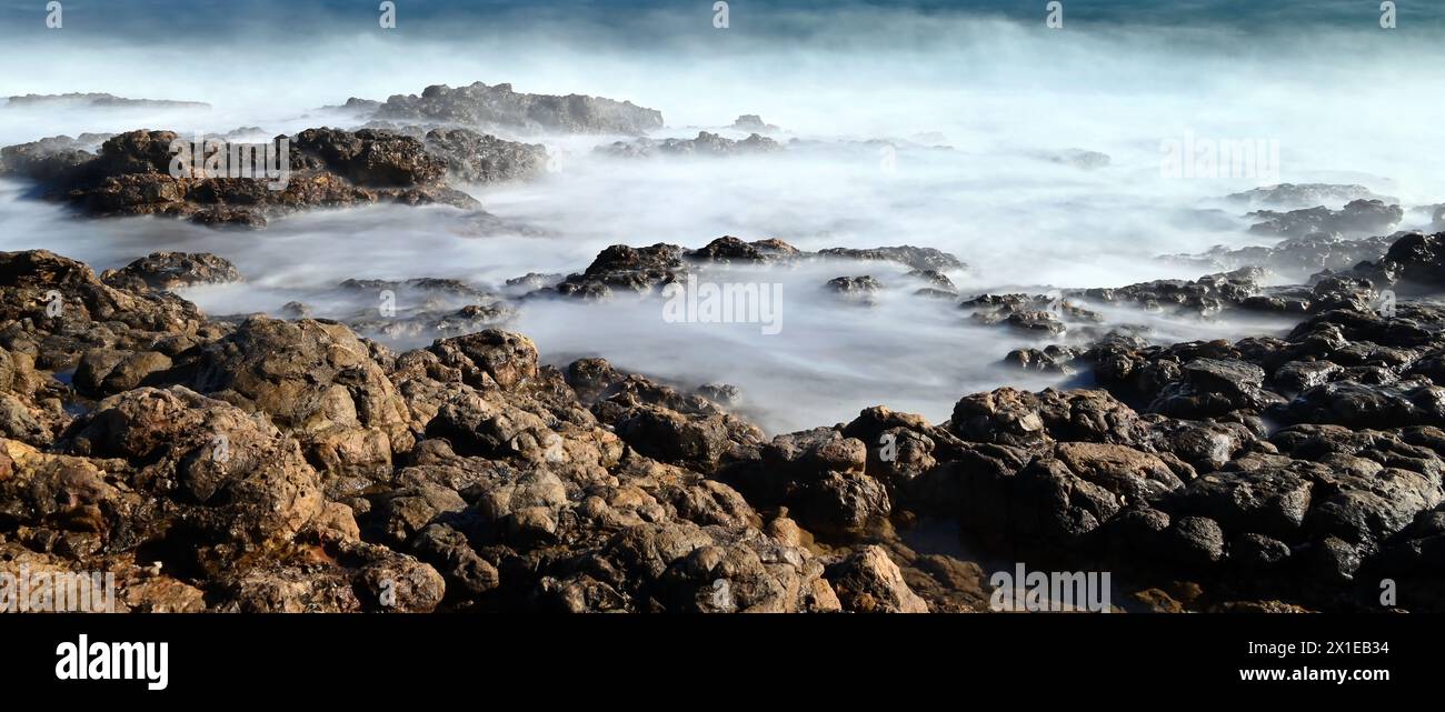 Onde nebbiose che si infrangono sulla costa rocciosa di Cap d'Antibes con esposizione prolungata in formato extra wide Foto Stock