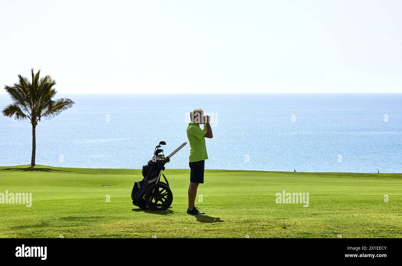 Il golfista misura con precisione la distanza dalla bandiera su un campo da golf con il telemetro laser. Sullo sfondo l'oceano. Foto Stock