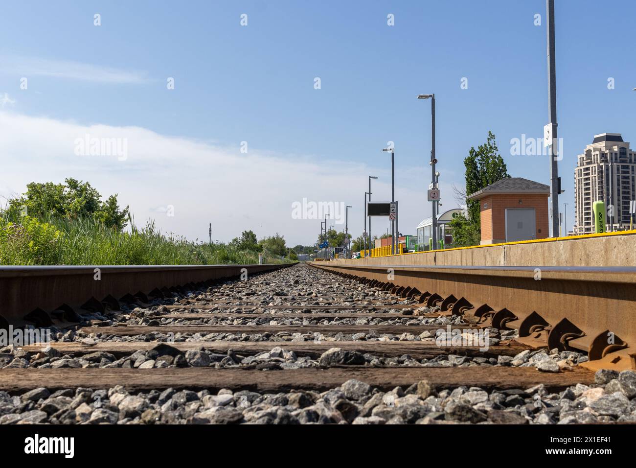 Binari ferroviari vuoti con linea di sicurezza gialla - circondati dal verde - cielo azzurro. Presa a Toronto, Canada. Foto Stock