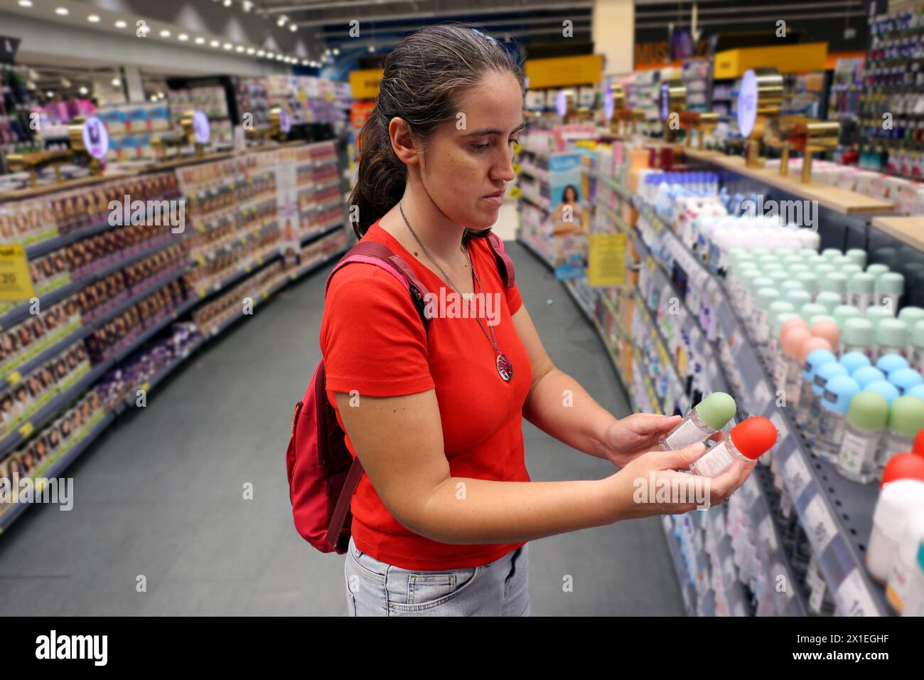 Una cliente donna è interessata al contenuto di deodorante per lo strato di ozono in un supermercato. Concetto di consumo, consumismo, inflazione Foto Stock