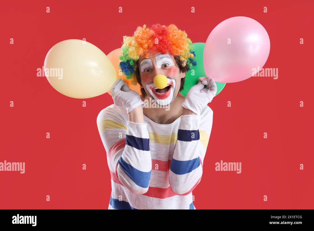Ritratto del clown con palloncini su sfondo rosso. Festa del giorno dello scemo d'aprile Foto Stock