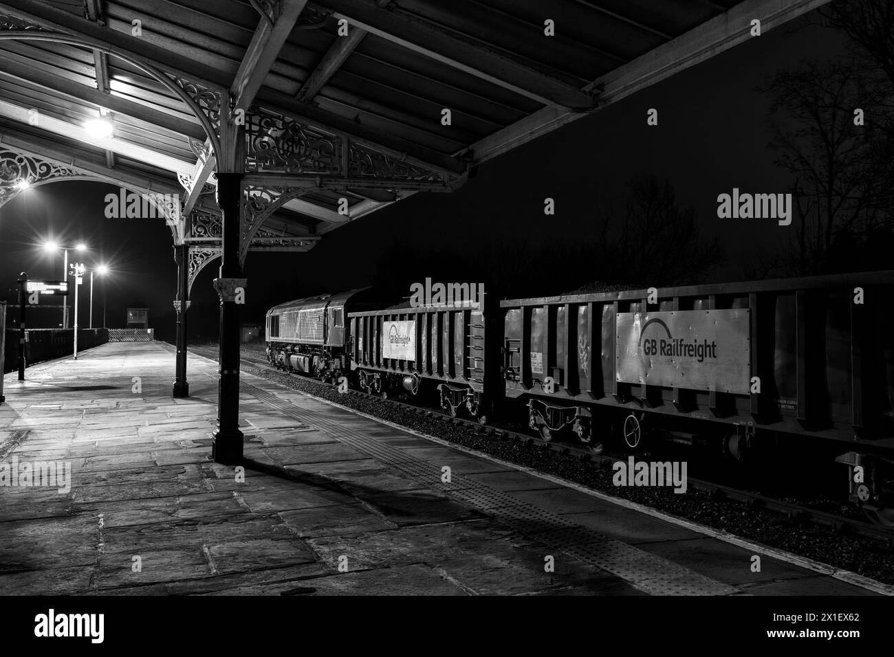 Locomotiva GB Rail Freight classe 66 66718 sotto la copertura della Midland Railway alla stazione ferroviaria di Hellifield con un treno che trasporta aggregati di notte Foto Stock