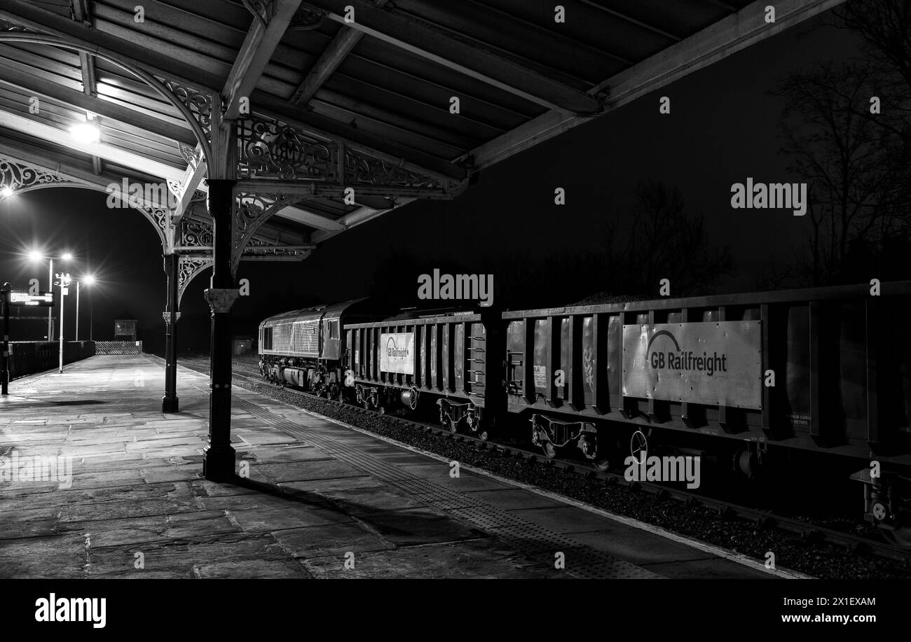 Locomotiva GB Rail Freight classe 66 66718 sotto la copertura della Midland Railway alla stazione ferroviaria di Hellifield con un treno che trasporta aggregati di notte Foto Stock