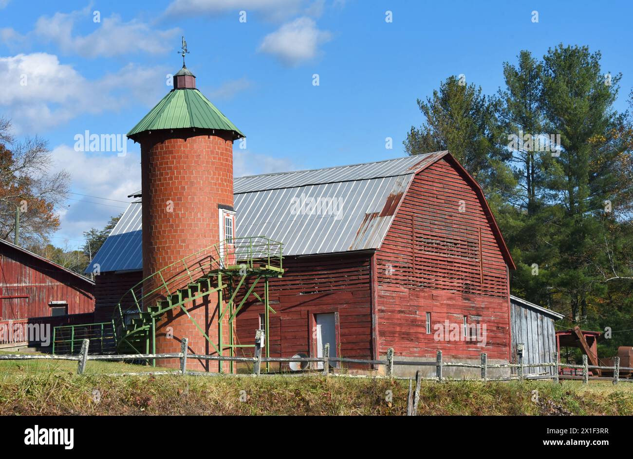 Un vecchio fienile rosso in legno ha accanto un silo rotondo in mattoni rossi. Il silo è coperto di verde. Le strutture si trovano nella Carolina del Nord. Foto Stock