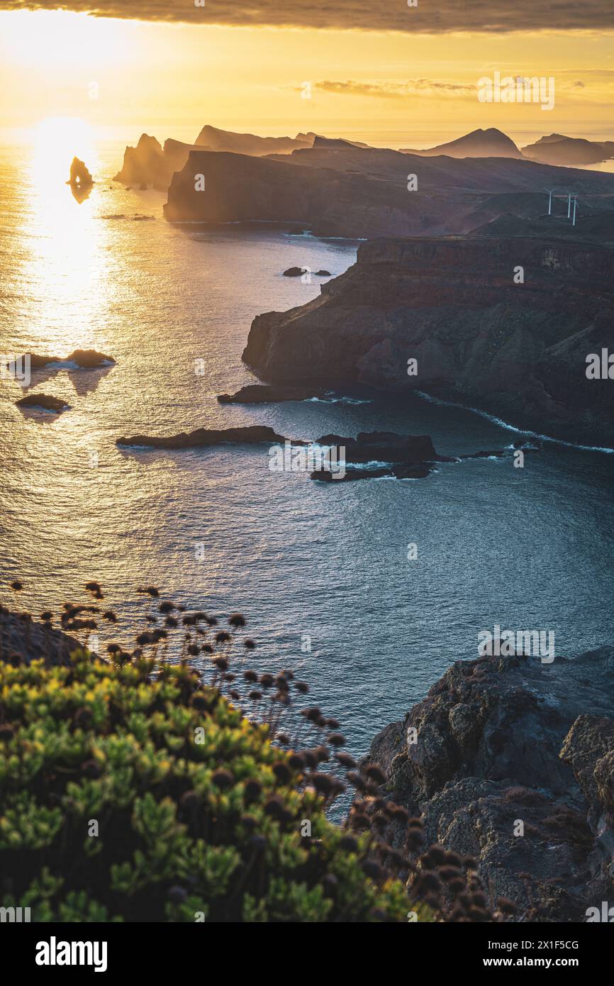 Descrizione: Magnifica alba dal punto panoramico su una ripida scogliera sopra il mare e lungo le aspre colline pedemontane della costa di Madeira con turbine eoliche Foto Stock