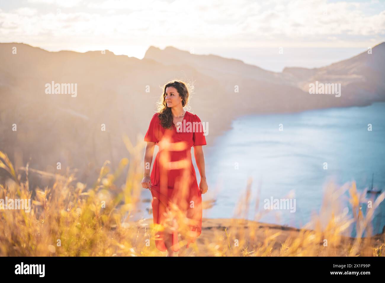 Descrizione: Donna in abito rosso cammina su un campo giallo godendosi il bagno di sole mattutino su un'isola vulcanica nell'Oceano Atlantico. São Lourento, Madeira I. Foto Stock