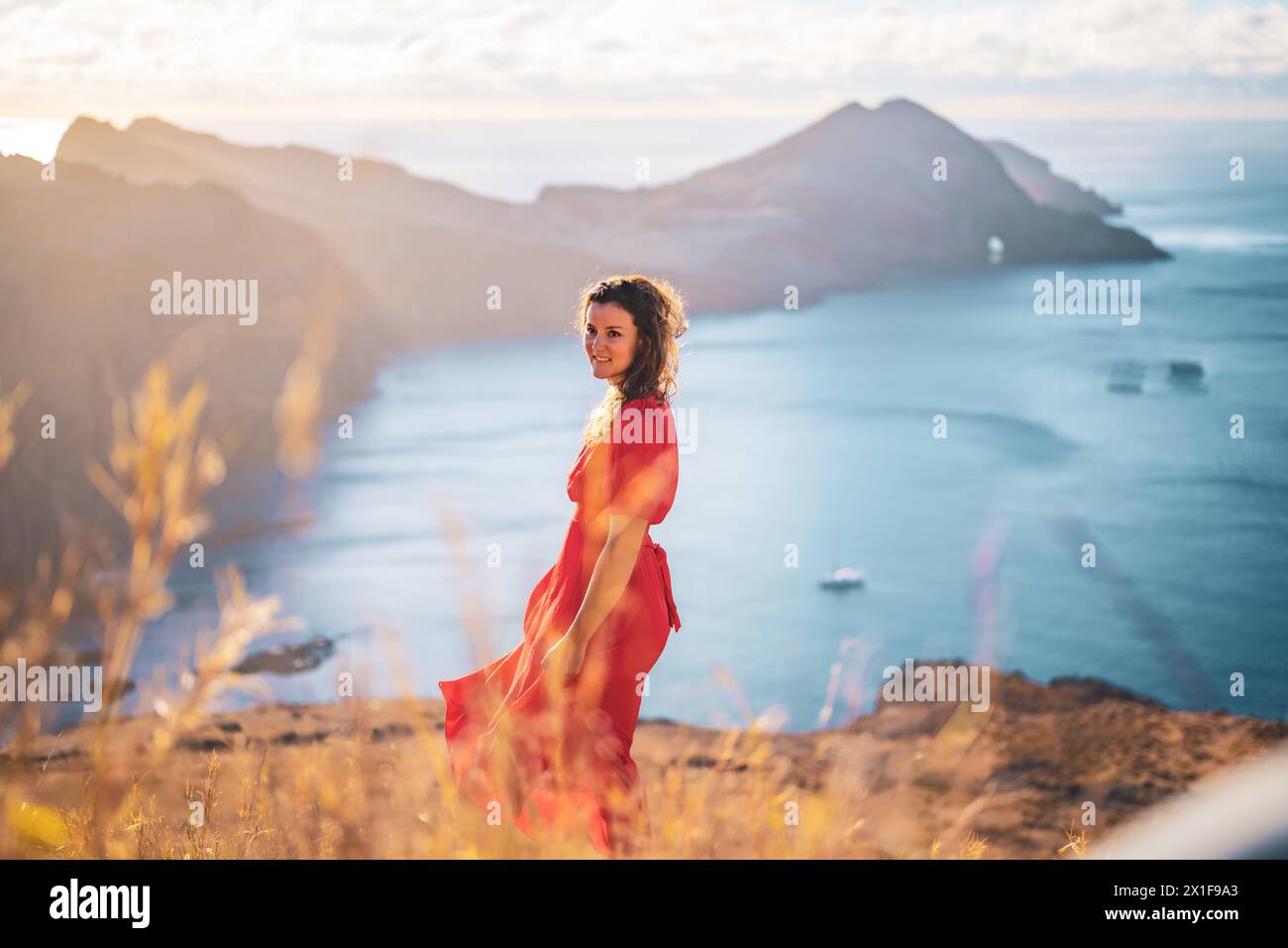 Descrizione: Vista laterale di una donna sorridente in abito rosso che si gode il bagno di sole mattutino su un'isola vulcanica nell'Oceano Atlantico. São Lourenceo, Madeira sì Foto Stock