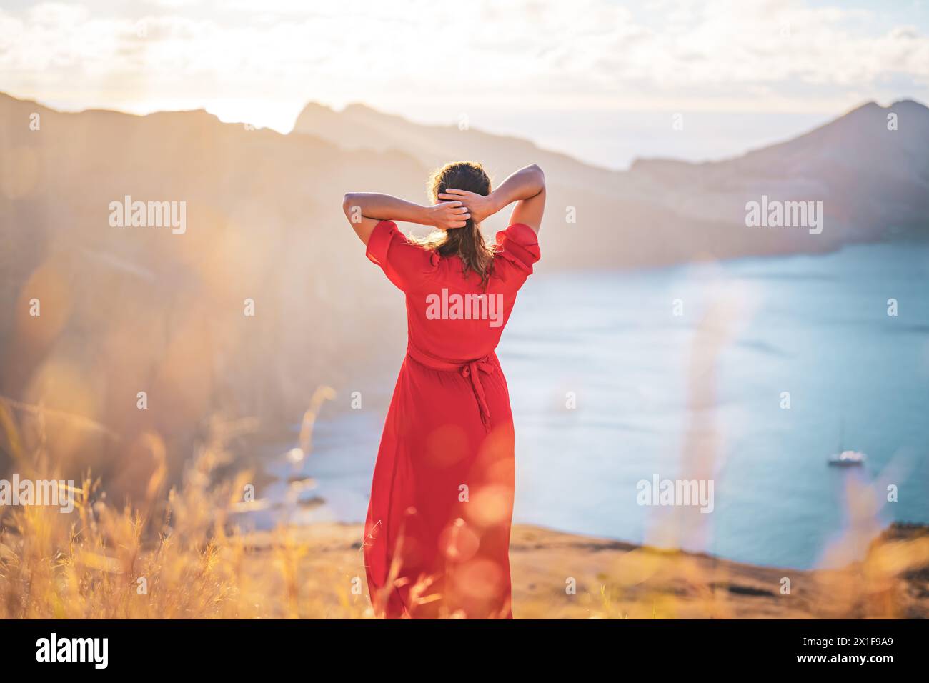 Descrizione: Vista posteriore di una donna in abito rosso che si gode il bagno di sole mattutino su un'isola vulcanica nell'Oceano Atlantico. São Lourento, Isola di Madeira, po Foto Stock