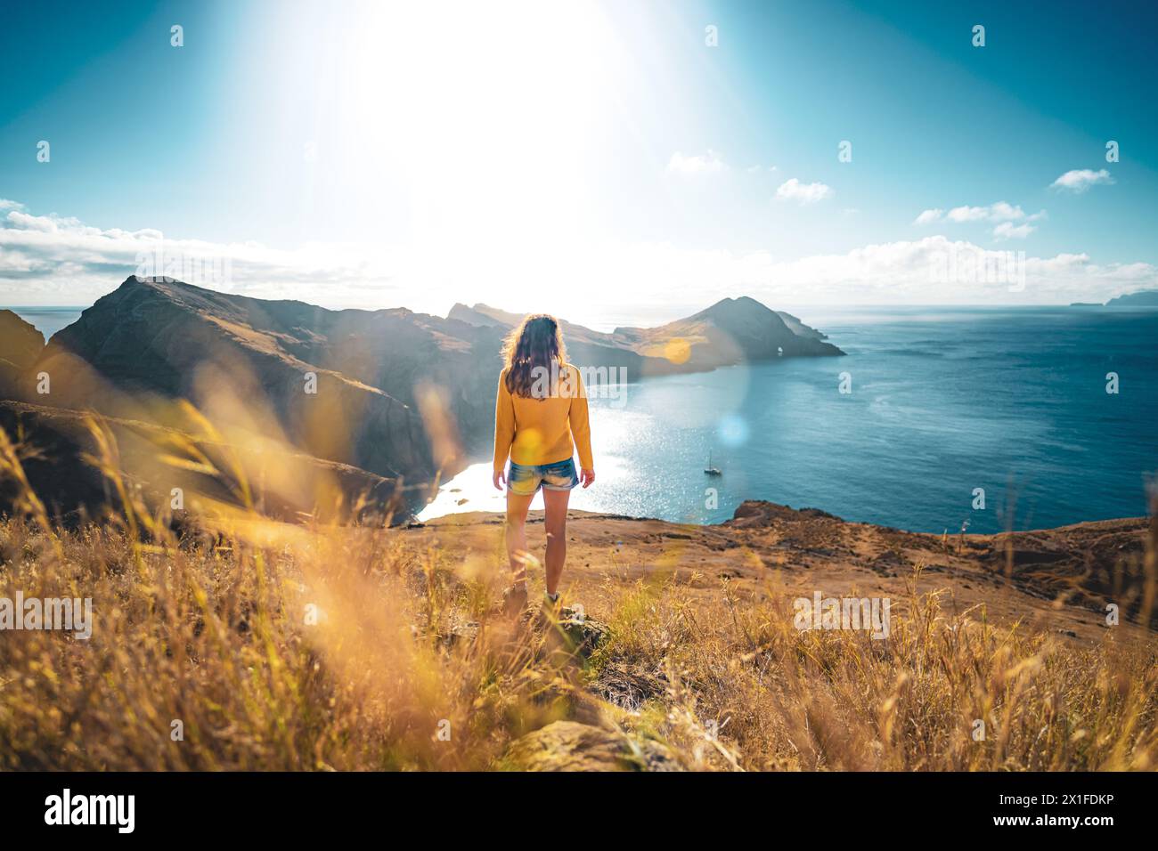 Descrizione: Vista posteriore di una donna turistica su una collina, che domina il paesaggio costiero dell'isola di Madeira nell'Oceano Atlantico al mattino. São Lou Foto Stock