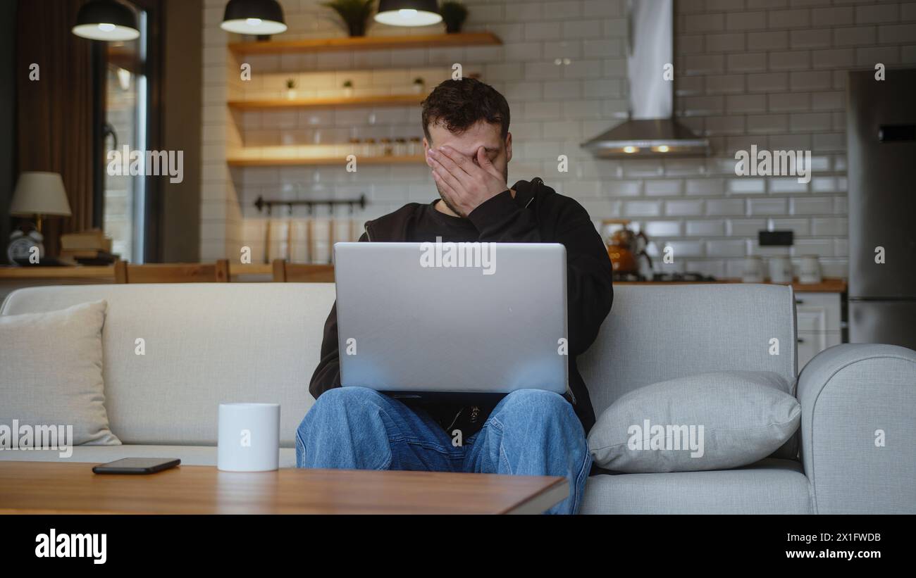 Un uomo frustrato seduto sul divano di casa, immettendo il numero di carta di credito sul laptop per acquistare la carta di credito online viene rifiutata o fuori limite, sentendosi triste e unha Foto Stock