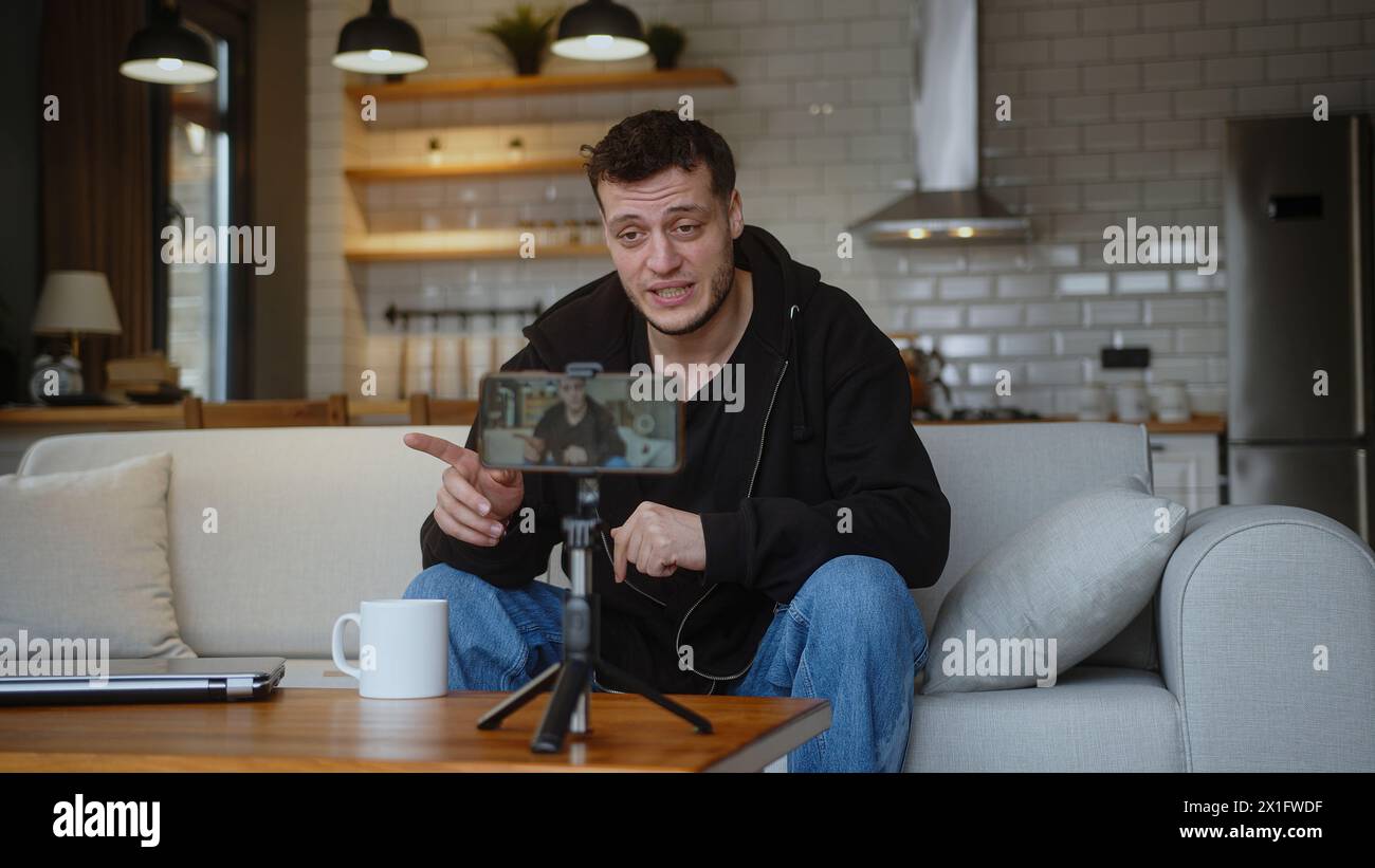 L'influencer vlogger si siede sul divano registrando video blog sul treppiede della fotocamera mobile parla per il canale multimediale personale, trasmettendo in streaming i blog delle sessioni live Foto Stock