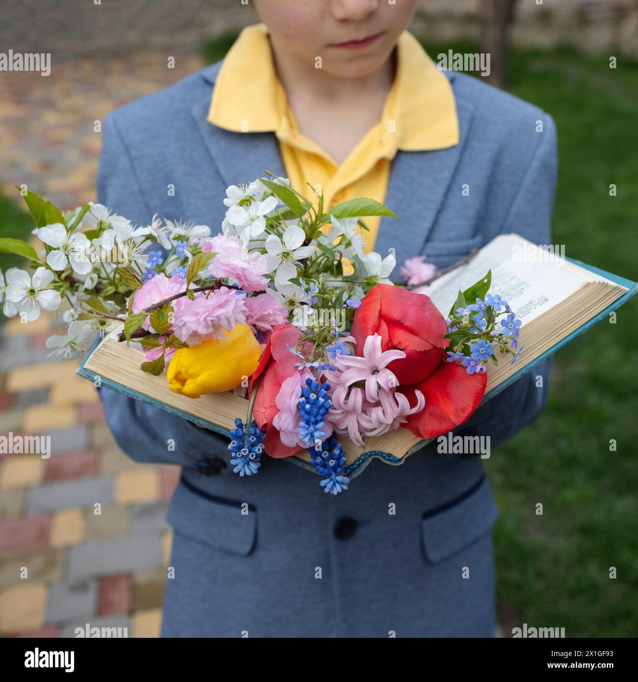 mazzo di fiori primaverili giace su pagine di libro aperto tenuto da bambino. Tempo di relax ed educazione. Atmosfera accogliente e poetica. Regalo per mamma da mamma Foto Stock