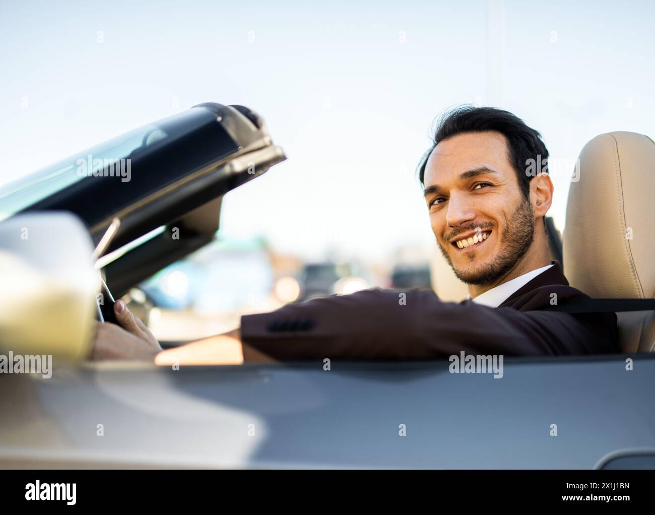 Un uomo d'affari sorridente gode di una giornata di sole seduto in una lussuosa cabriolet Foto Stock
