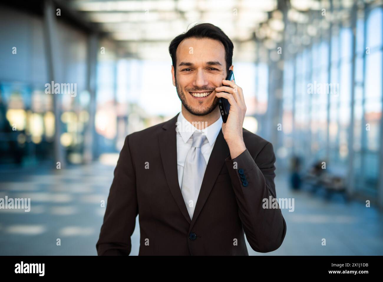Giovane uomo d'affari allegro che parla al telefono cellulare in un ambiente moderno Foto Stock