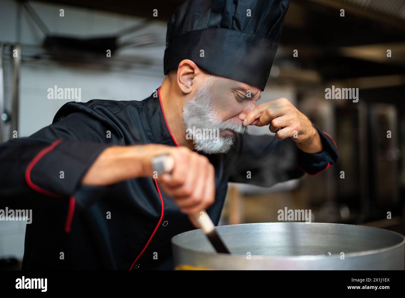 Chef senior specializzato con un test del gusto mentre cucina in una cucina commerciale Foto Stock