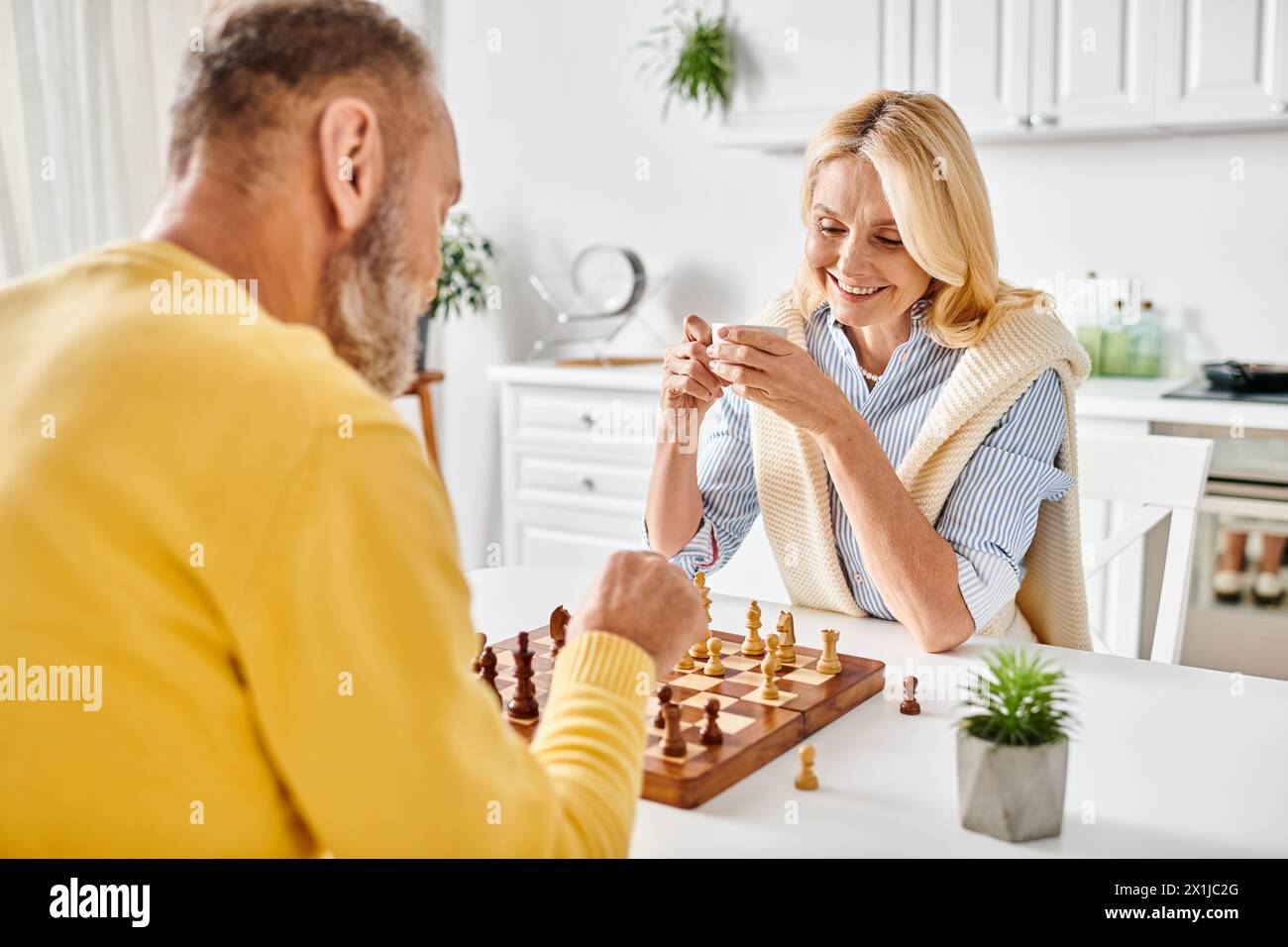 Una coppia matura di intimi articoli per la casa impegnata in una partita a scacchi, concentrandosi intensamente sul tabellone mentre pianificano le loro mosse successive. Foto Stock