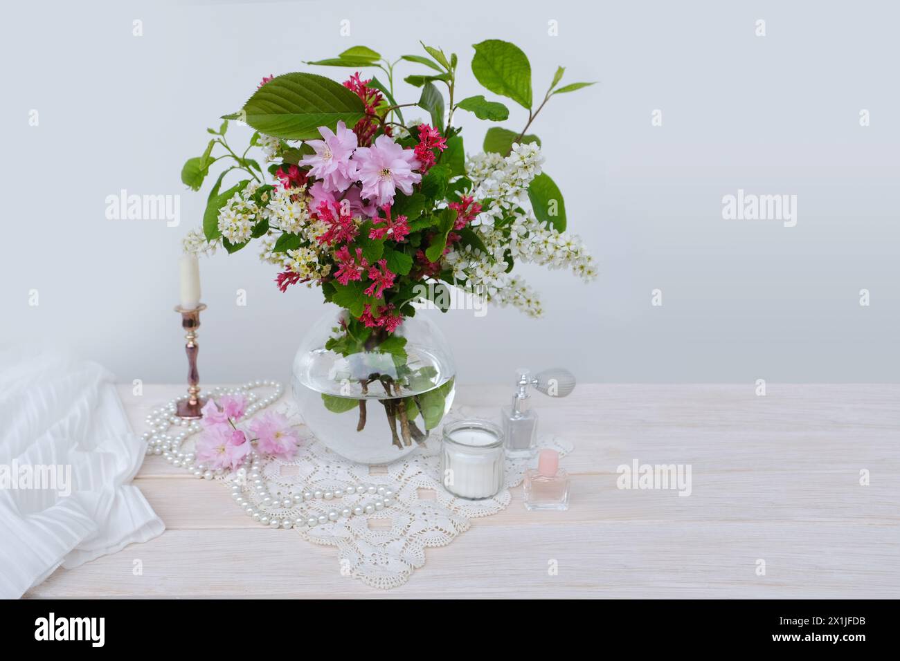 bouquet vibrante di ciliegio fiorito in vaso di vetro sul tavolo, ciliegio di uccello, candele, boudoir per signora, creando stile retrò ed eleganza Foto Stock