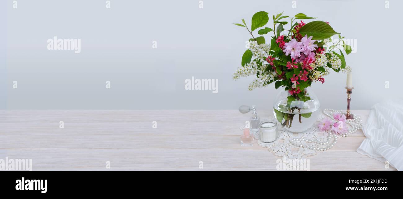 panorama vivace bouquet di ciliegio in fiore in vaso di vetro sul tavolo, ciliegia di uccello, candele, boudoir per signora, creando stile retrò ed eleganza Foto Stock
