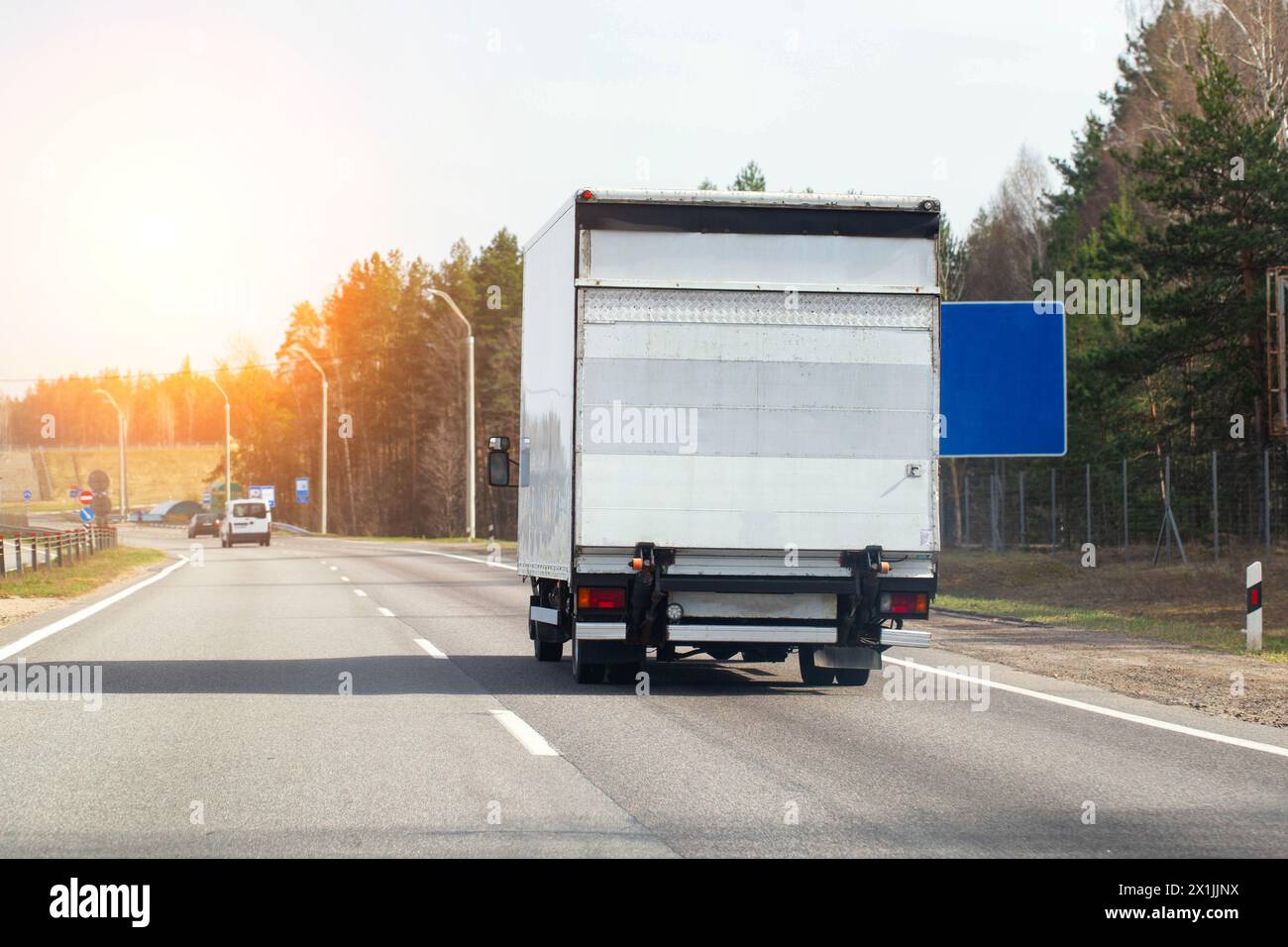 Un moderno pulmino con sponda montacarichi guida lungo una strada asfaltata sullo sfondo di un tramonto. Concetto di trasporto su strada di autocarri con li idraulici Foto Stock