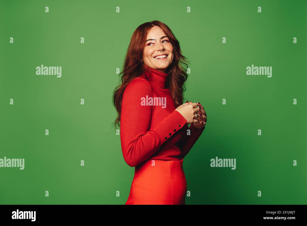 Donna alla moda anni '20 con sfondo verde vivace in studio, indossa abiti casual e un pullover elegante. Indossando un naso e un anello con setto, trasuda carefr Foto Stock