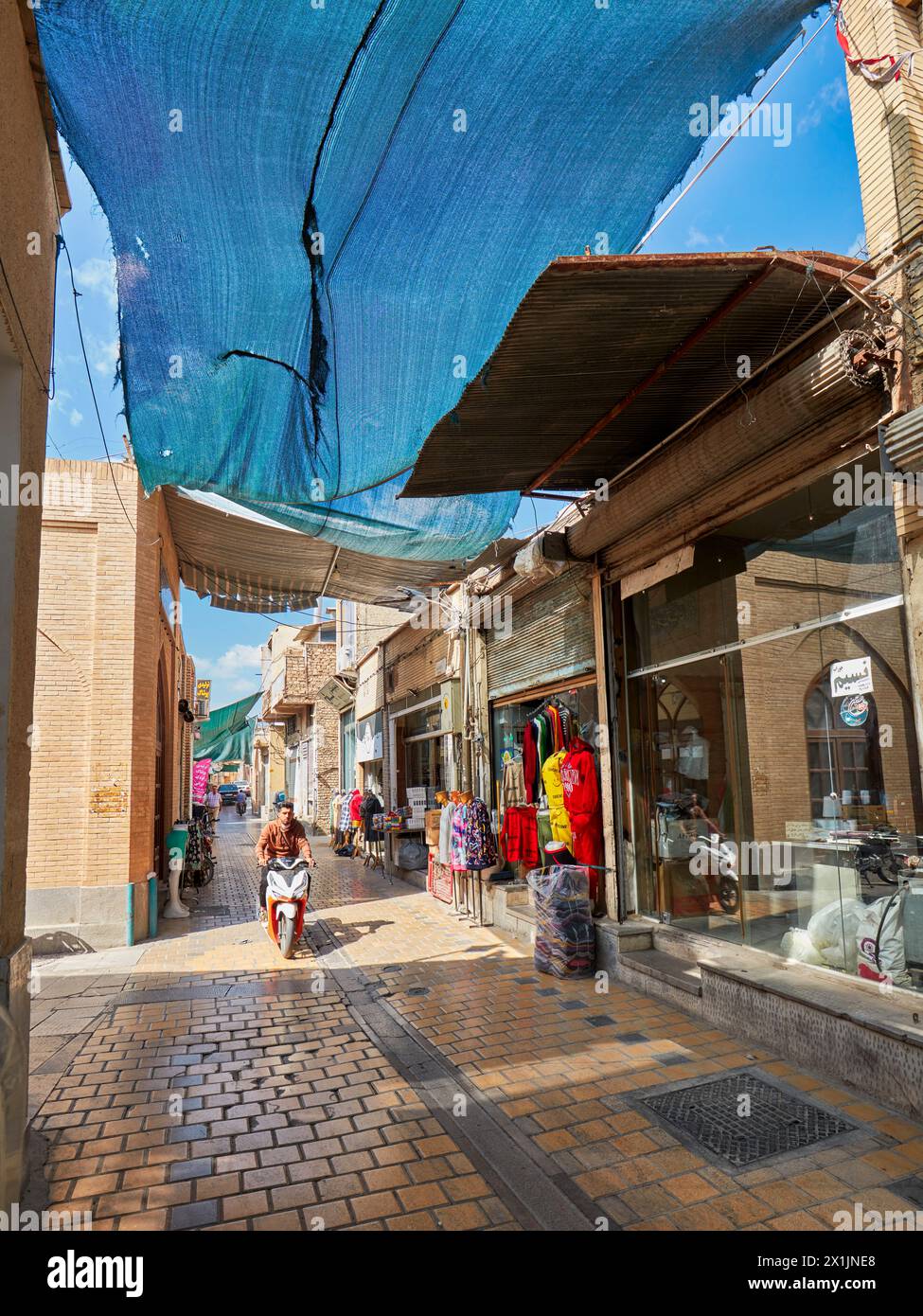 Una stretta strada acciottolata con tettoia parasole fiancheggiata da piccoli negozi nel centro storico di Isfahan, Iran. Foto Stock