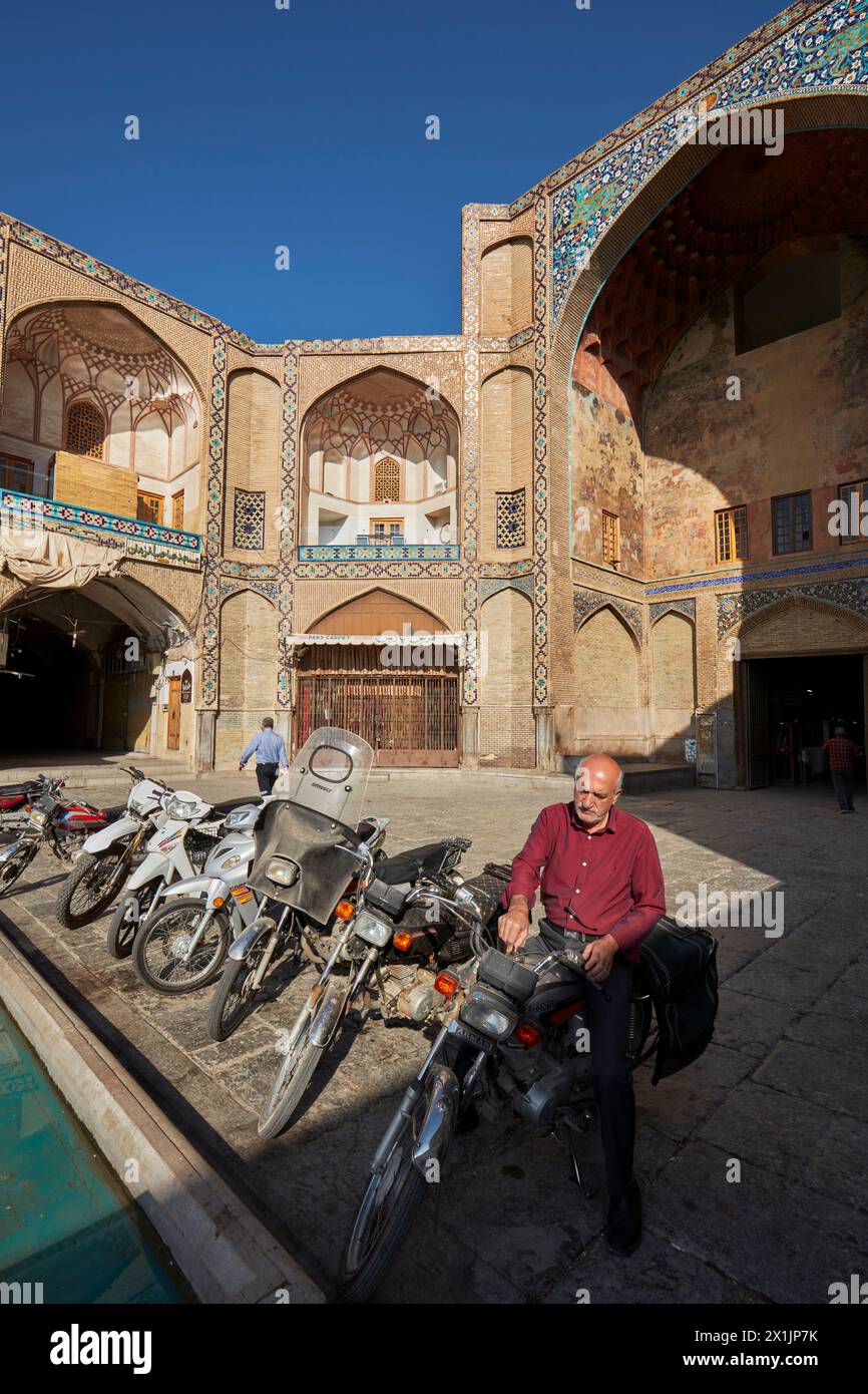 Un uomo gira la chiave per avviare il motore della sua moto parcheggiata alla porta di Qeysarie, la porta d'ingresso al Grand Bazaar in Piazza Naqsh-e Jahan. Isfahan, Iran. Foto Stock