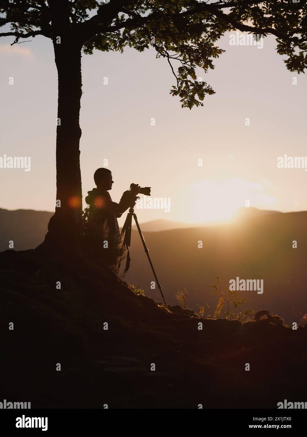 Una silhouette per fotografi di paesaggi con treppiede e fotocamera al tramonto in un paesaggio montano dalle pendici minimali. Foto Stock