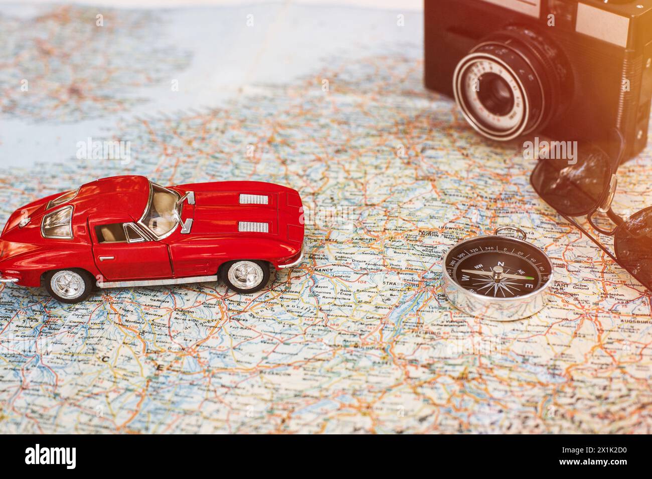 Viaggiare in auto. Vintage rosso auto giocattolo, Fotocamera, Bussola e occhiali da sole giacente sulla mappa Foto Stock