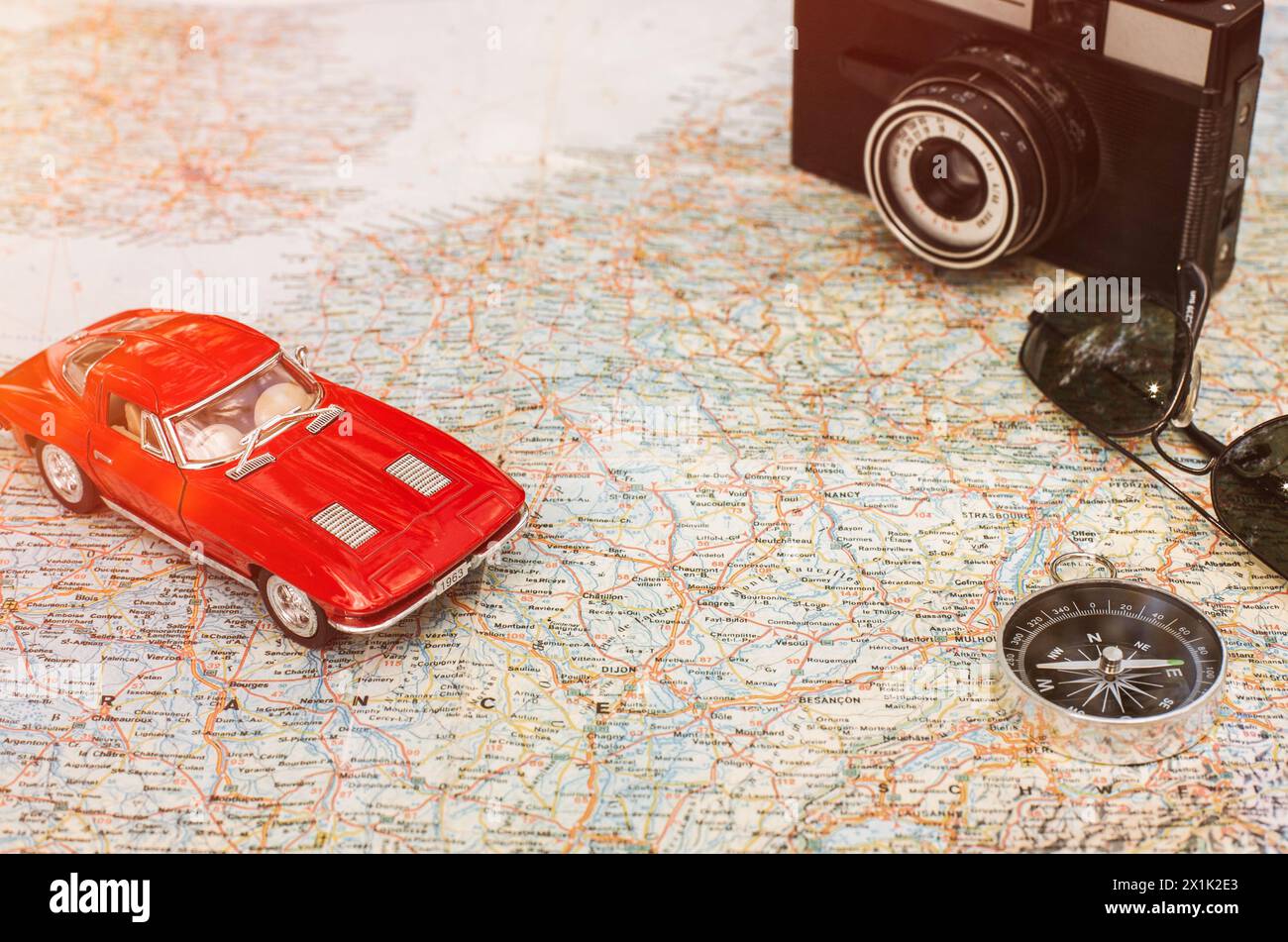 Viaggiare in auto. Vintage rosso auto giocattolo, Fotocamera, Bussola e occhiali da sole giacente sulla mappa Foto Stock