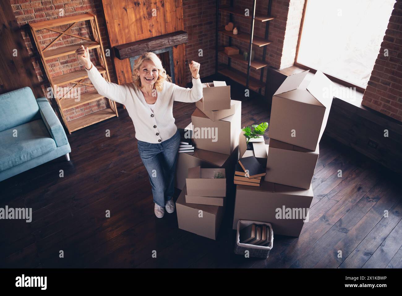 Ritratto a grandezza naturale della signora anziana alzare i pugni di successo indossa cardigan bianco loft interno casa interna Foto Stock