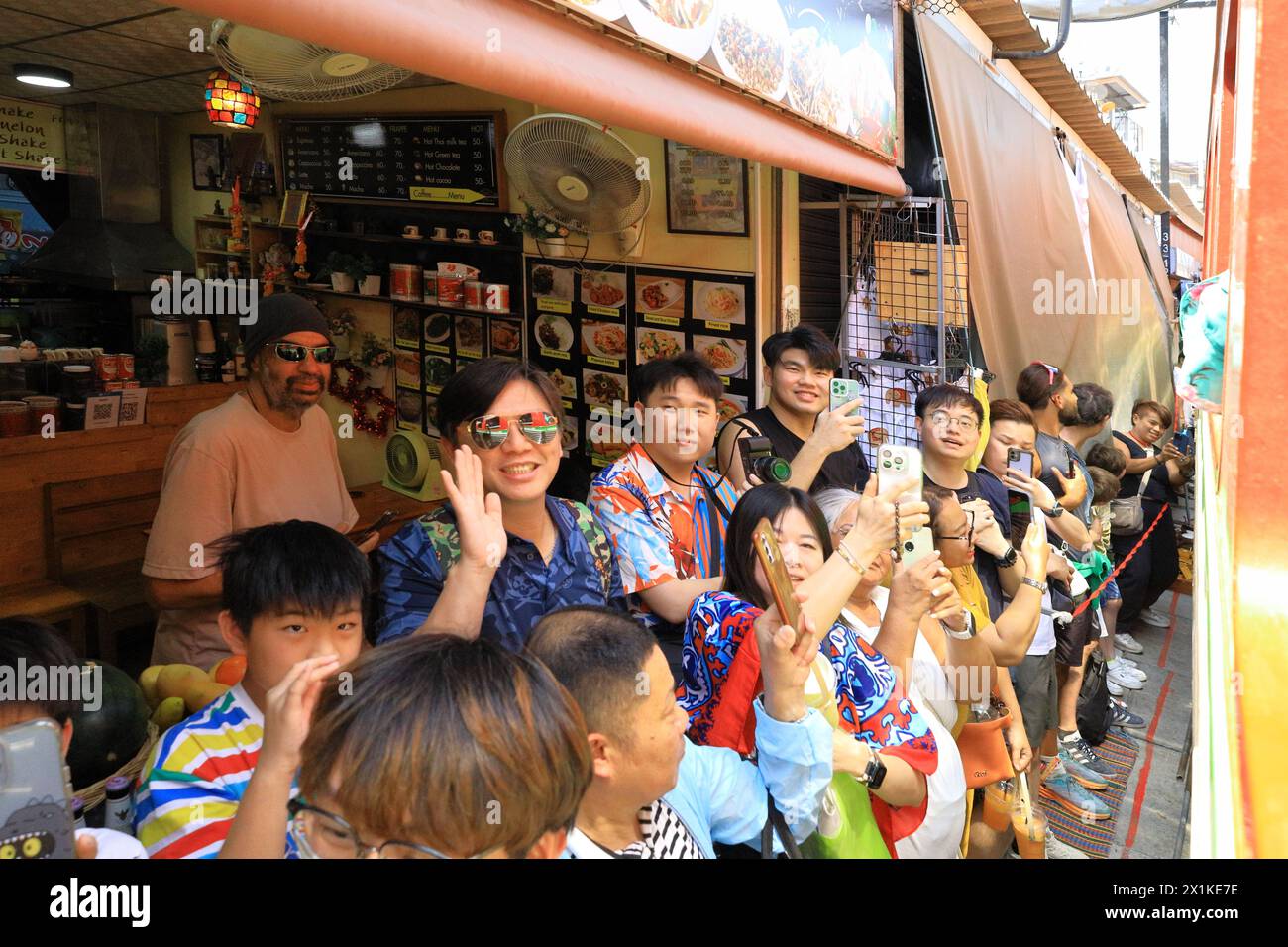 Maeklong, Thailandia - turisti che usano il loro smartphone per catturare il treno che passa attraverso il mercato dei treni molto vicino alle bancarelle Foto Stock