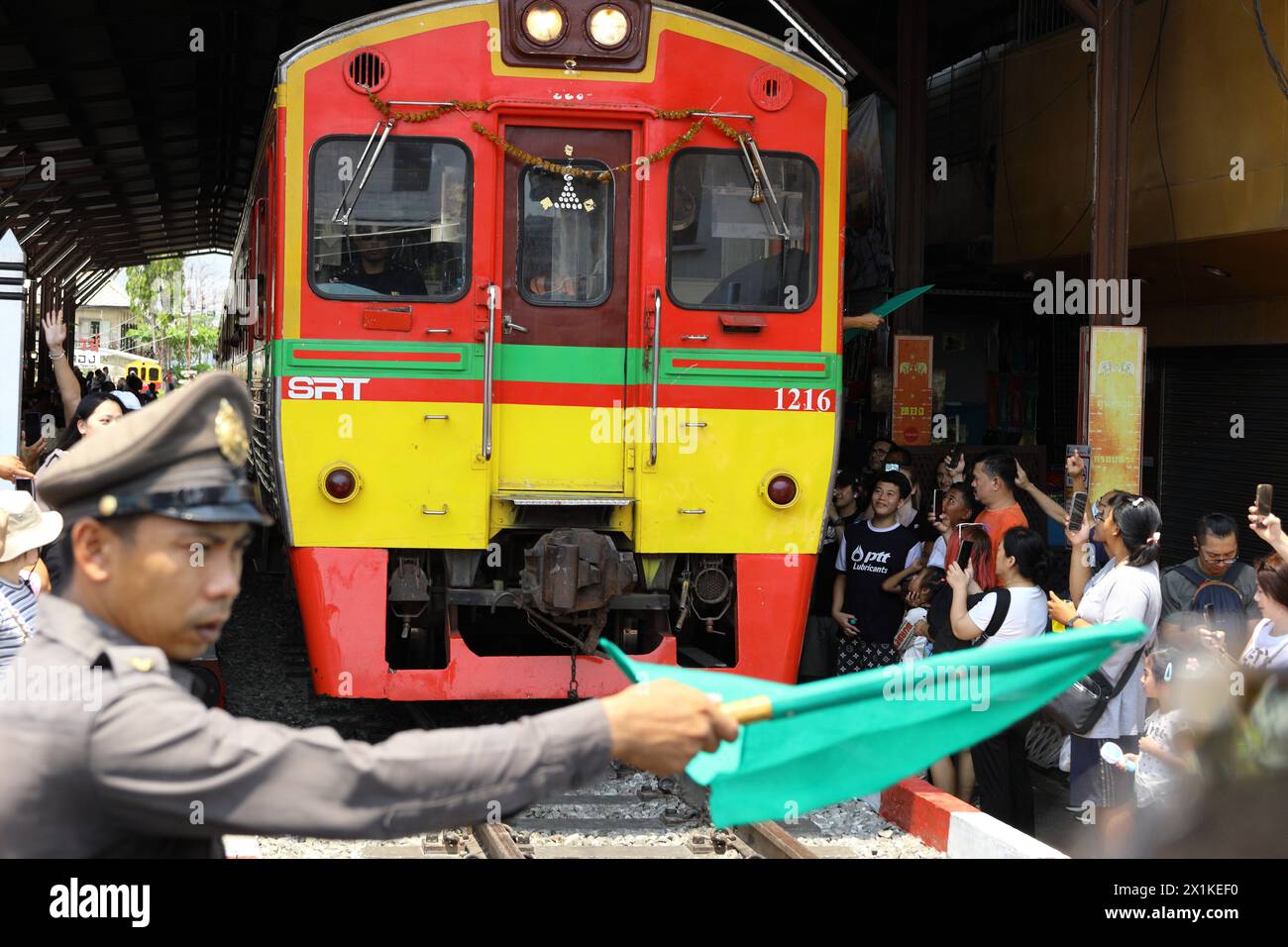 Maeklong, Thailandia - il poliziotto controlla la folla e il traffico quando i treni escono dalla stazione ed entrano nel mercato dei treni molto vicino alle bancarelle Foto Stock