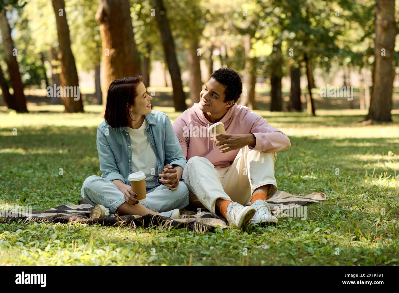 Una coppia variegata in un abbigliamento vivace che si gode un pomeriggio piacevole su una coperta in un parco. Foto Stock