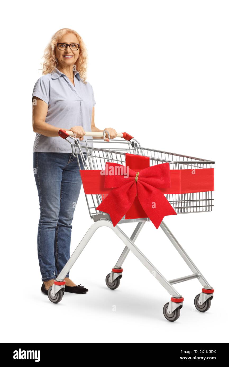 Donna matura in piedi con un carrello della spesa vuoto decorato con un fiocco rosso isolato su sfondo bianco Foto Stock