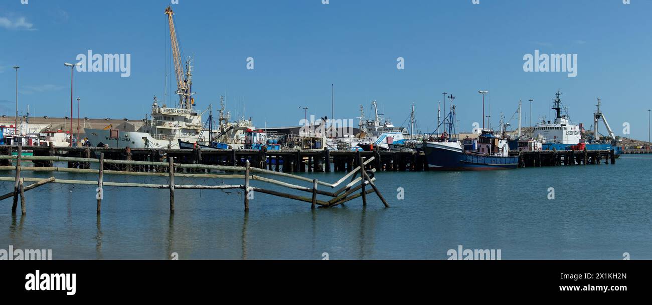 Panorama delle navi e delle imbarcazioni ormeggiate nel porto di Luderitz in Namibia con una staccionata in legno in primo piano. Foto Stock