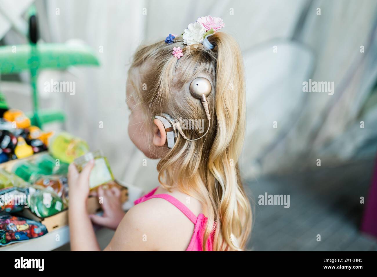 Il bambino cammina con l'apparecchio acustico per impianti cocleari in strada estiva. Inclusione e tecnologie moderne per il trattamento della perdita dell'udito. Copia spazio Foto Stock