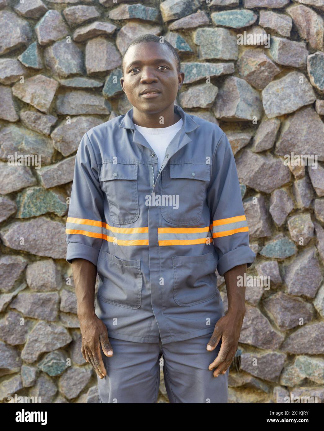 giovane africano con un grande sorriso e abbigliamento da lavoro, sfondo in pietra da parete Foto Stock