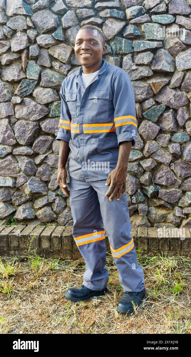 giovane operaio africano in abbigliamento da lavoro, parete di pietra sullo sfondo Foto Stock