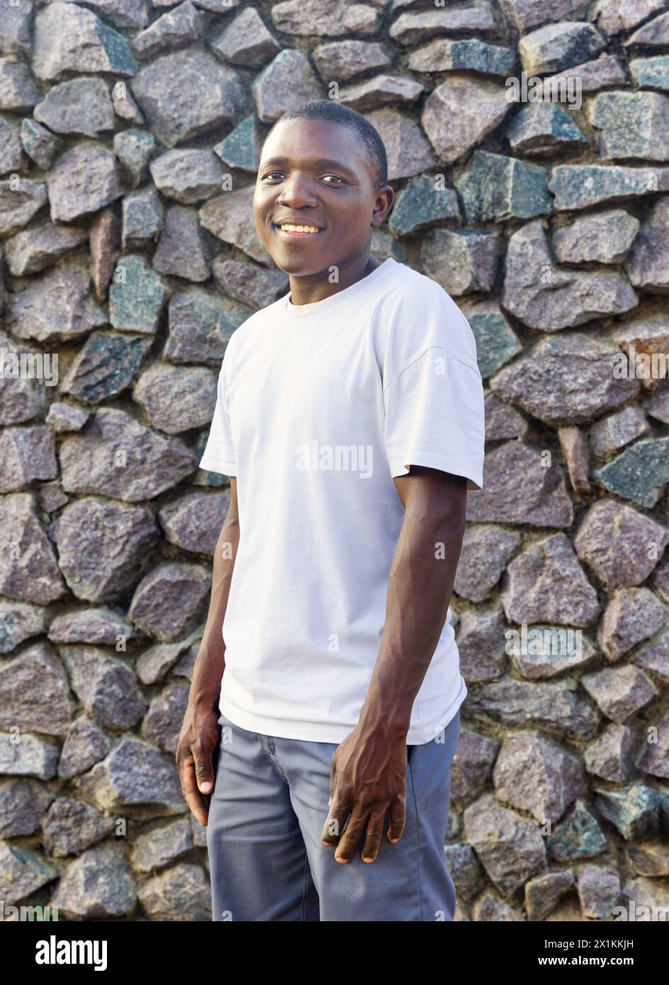 giovane africano con un grande sorriso e t-shirt bianca, abbigliamento casual, sfondo in pietra da parete Foto Stock