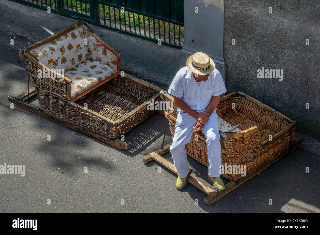 Uomo che indossa una barca di paglia seduto su una tradizionale slitta con cesti di vimini a Monte Funchal, isola di Madeira, Portogallo Foto Stock