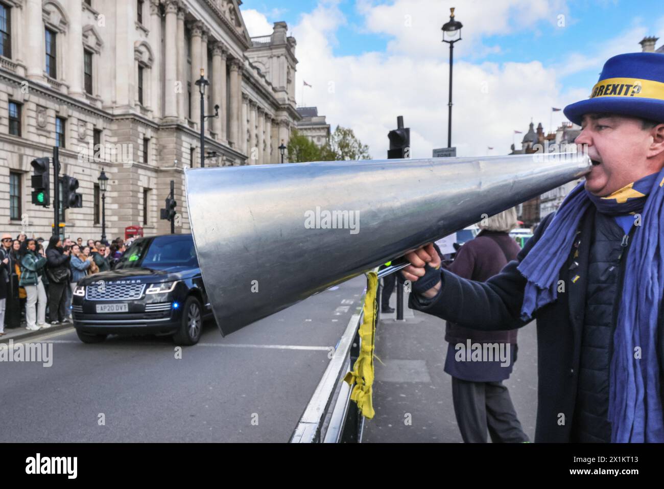 Londra, Regno Unito. 17 aprile 2024. Steve Bray, meglio conosciuto come "Stop Brexit Man" di Westminster, grida all'auto del PM con il suo megafono proprio mentre il corteo di Rishi Sunak li passa davanti per il PM per partecipare ai PMQ al Parlamento. A un certo punto, il megafono sembra "ingoiare" l'auto del PM in una divertente illusione ottica. Crediti: Imageplotter/Alamy Live News Foto Stock