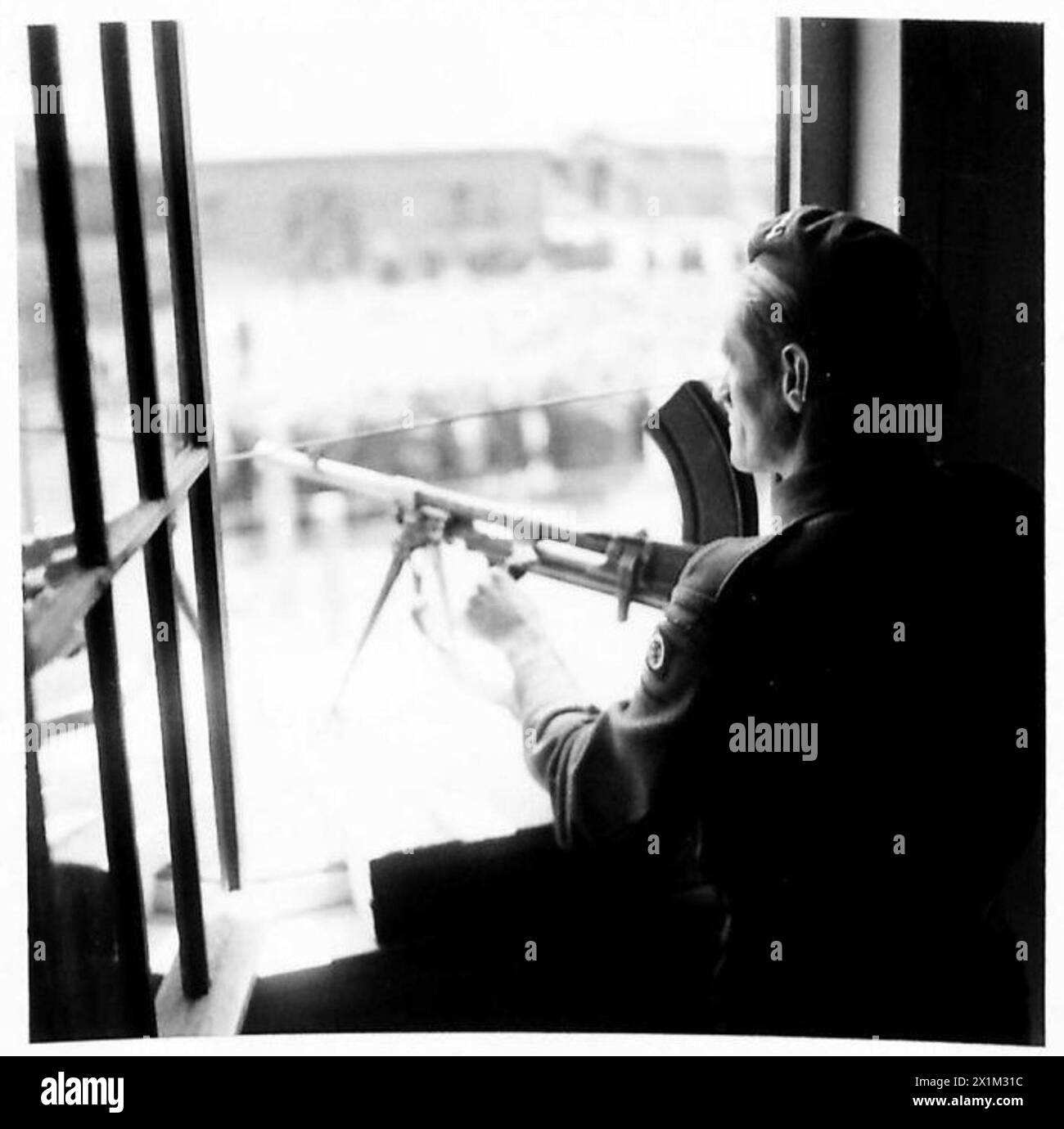 Gunner Wright della 15th Scottish Division tiene d'occhio con una pistola Bren da una finestra al piano superiore che si affaccia sulle gabbie della prigione, illustrando il ruolo degli osservatori nel mantenere la sicurezza durante le operazioni. Foto Stock