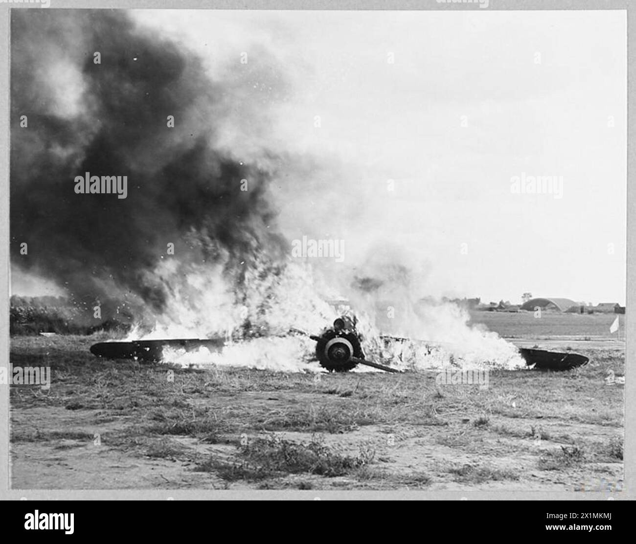 I vigili del fuoco della Royal Air Force dimostrano nuove tecniche per combattere gli incendi di aerei e benzina in un campo di aviazione, 1943. Fumo e fiamme sorgono da un aereo schiantato, come osservano gli esperti. Foto Stock