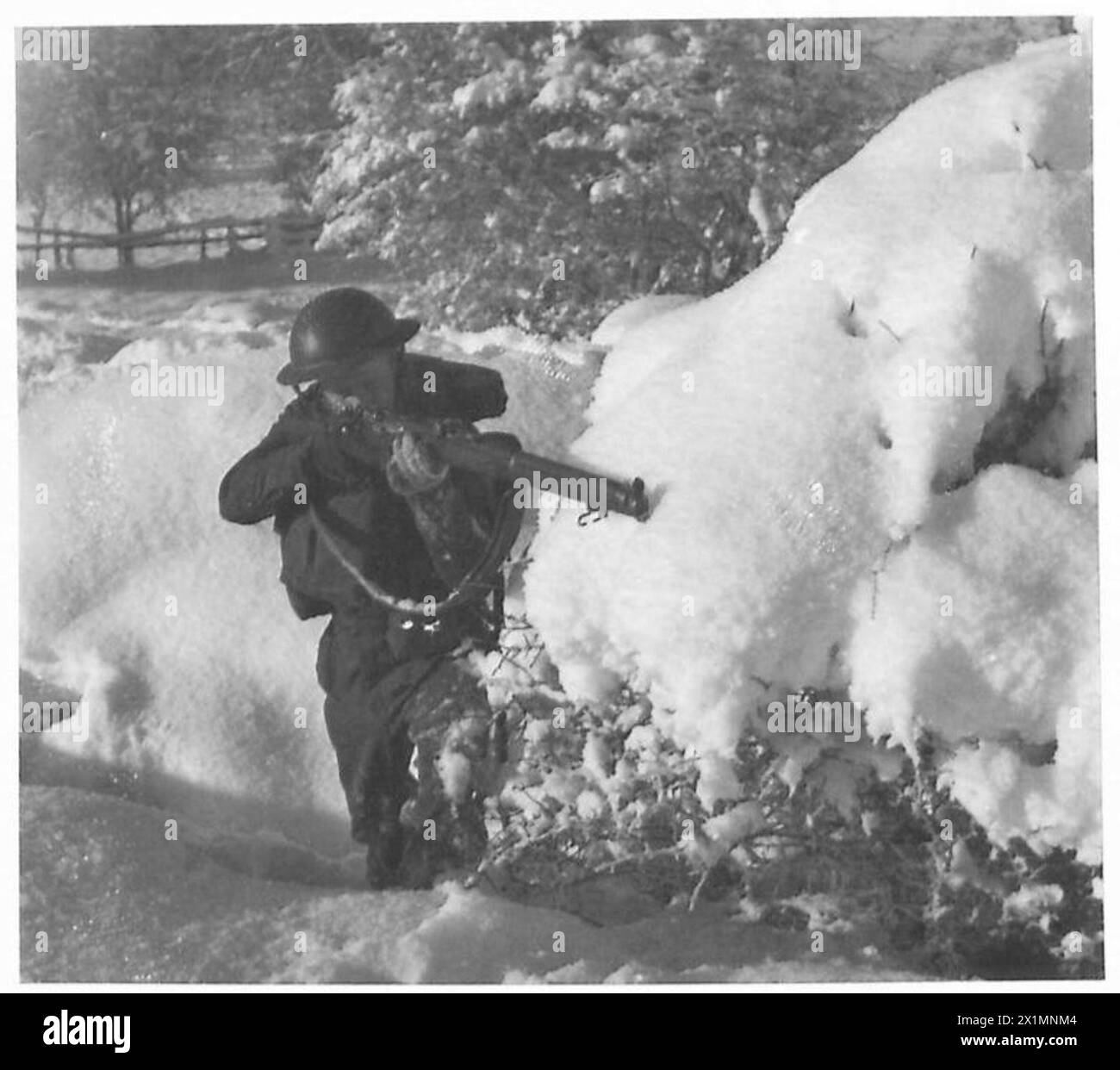 Un soldato dell'esercito britannico mira da dietro un cespuglio innevato in un ambiente invernale. Foto Stock