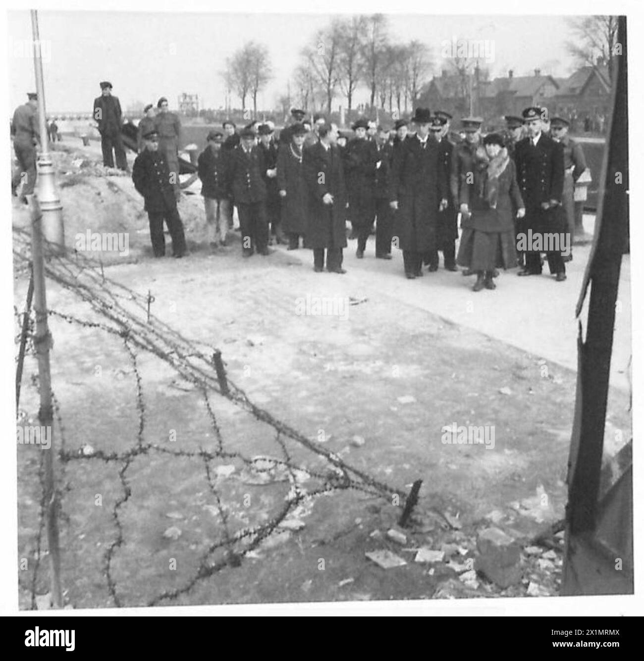 La regina visita un sito della riva del canale dove sono stati uccisi i custodi delle chiuse, posizionando una rosetta su una pietra. Una sopravvissuta con un braccio in una fionda cammina accanto a lei durante le operazioni dell'esercito britannico sotto il 21st Army Group. Foto Stock
