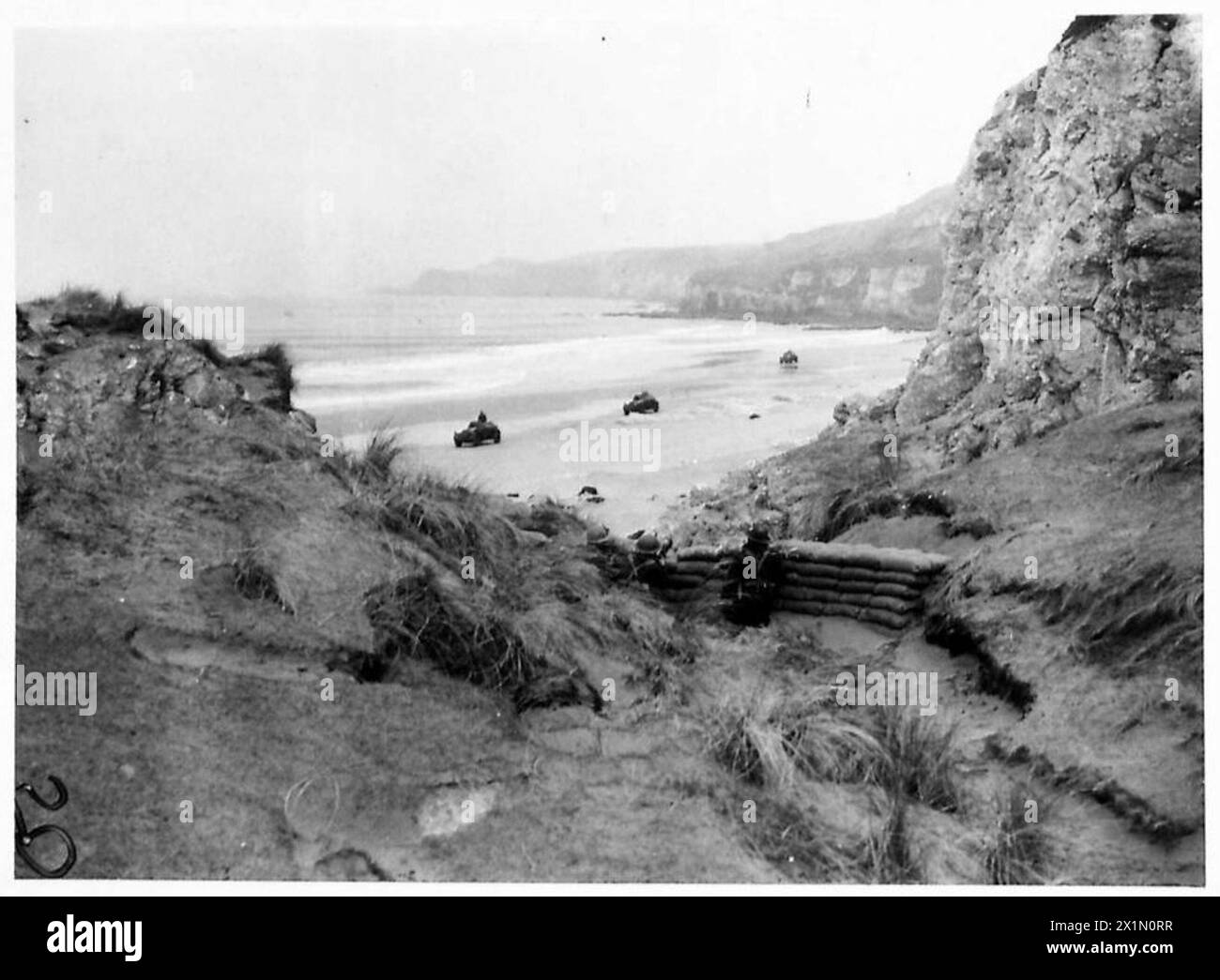 Le auto blindate pattugliano la costa dell'Irlanda del Nord mentre una pattuglia occupa una posizione difensiva, illustrando le operazioni di sicurezza costiera da parte delle forze dell'esercito britannico. Foto Stock