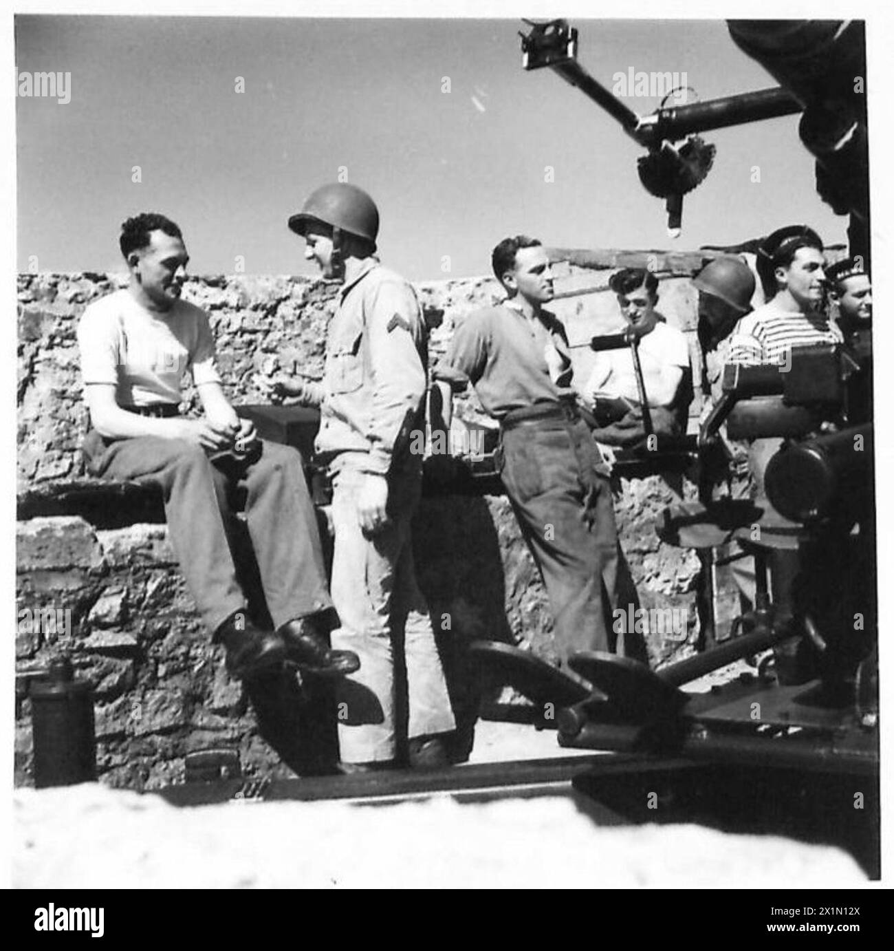 I cannoni britannici, americani e francesi interagiscono durante una pausa nelle operazioni di difesa del forte, posizionate vicino a un cannone Bofors. Foto Stock